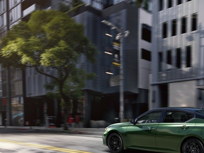 Nissan Altima verde 2026 en movimiento por ciudad, llantas negras, techo oscuro y fondo urbano desenfocado que resalta su diseño dinámico.