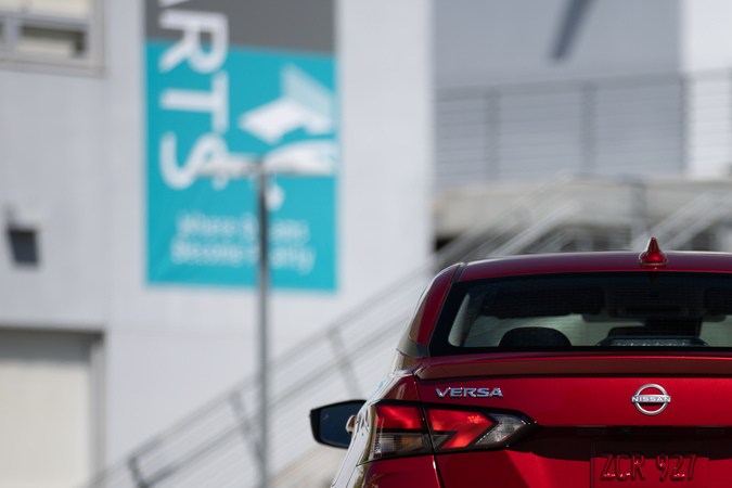 Vista trasera del Nissan Versa 2025 rojo, destacando el diseño de las luces posteriores, el emblema y la defensa deportiva en un entorno urbano.