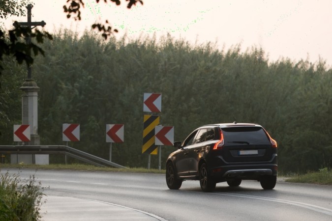 Un coche negro entra en un giro brusco durante el anochecer de principios de otoño, cruza en el fondo, la importancia de la conducción cuidadosa y la precaución en la carretera para evitar accidentes.
