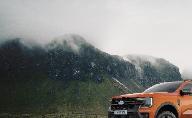 Ford Ranger 2026 Wildtrak PHEV naranja, pickup híbrida enchufable todoterreno en carretera mojada, enfocada en off-road y estilo deportivo.