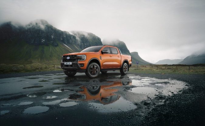 Ford Ranger 2026 Wildtrak PHEV naranja, pickup híbrida enchufable todoterreno en carretera mojada, enfocada en off-road y estilo deportivo.