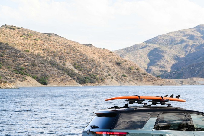 Vista lateral Nissan Pathfinder 2026 junto a lago, con tablas en el techo, destacando diseño SUV para aventura familiar.