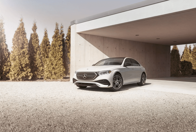 Mercedes‑Benz E450 2025 blanco frente a casa minimalista, sedán de lujo premium, vista tres cuartos frontal.
