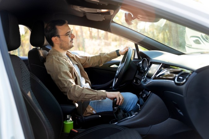 Hombre conduciendo un coche moderno, disfrutando de un día soleado en la carretera, mostrando prácticas de conducción segura y operación del vehículo