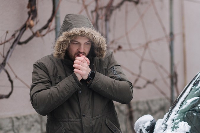 Un hombre guapo limpia su auto de la nieve usando las manos. El invierno al aire libre