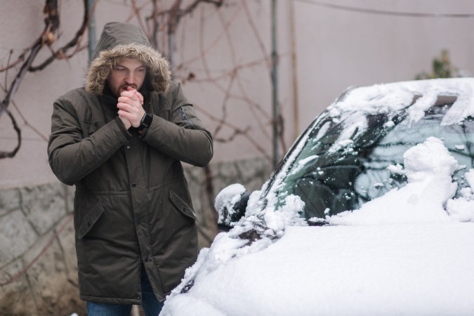Un hombre guapo limpia su auto de la nieve usando las manos. El invierno al aire libre
