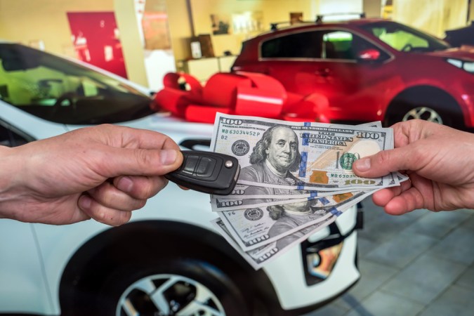 empresario compra un auto nuevo en la sala de espectáculos dando dinero y tomando llaves del auto, concepto de finanzas