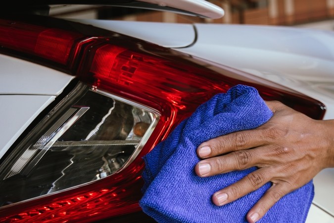 Un limpiador profesional de automóviles que lava meticulosamente un vehículo brillante con una manguera de presión y espuma. El hombre se enfoca en el exterior del automóvil, asegurando un acabado impecable y pulido en una estación de detalles automática
