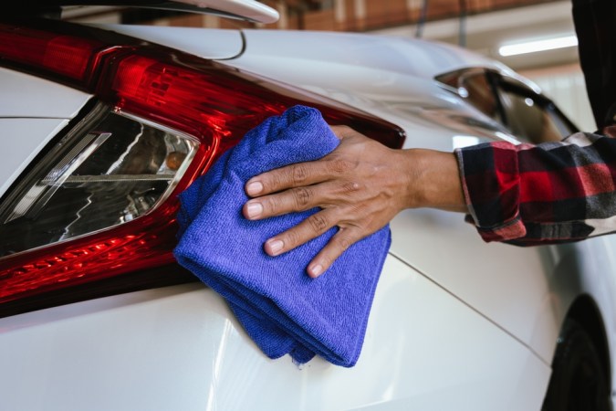 Un limpiador profesional de automóviles que lava meticulosamente un vehículo brillante con una manguera de presión y espuma. El hombre se enfoca en el exterior del automóvil, asegurando un acabado impecable y pulido en una estación de detalles automática