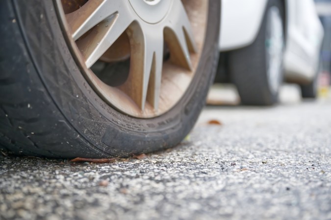 Primer plano de un neumático de coche bastante pinchado. El borde está cubierto de suciedad y humedad.
