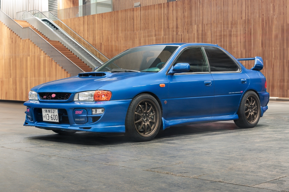 Subaru Impreza azul generación antigua, versión deportiva sedán con alerón grande en interior moderno.