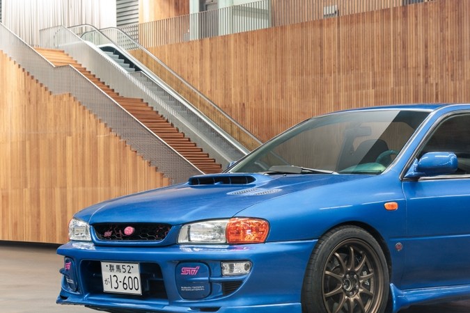 Subaru Impreza azul generación antigua, versión deportiva sedán con alerón grande en interior moderno.