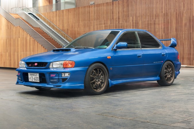 Subaru Impreza azul generación antigua, versión deportiva sedán con alerón grande en interior moderno.