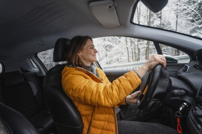 Joven caucásica feliz conduciendo auto en invierno en el bosque, retrato