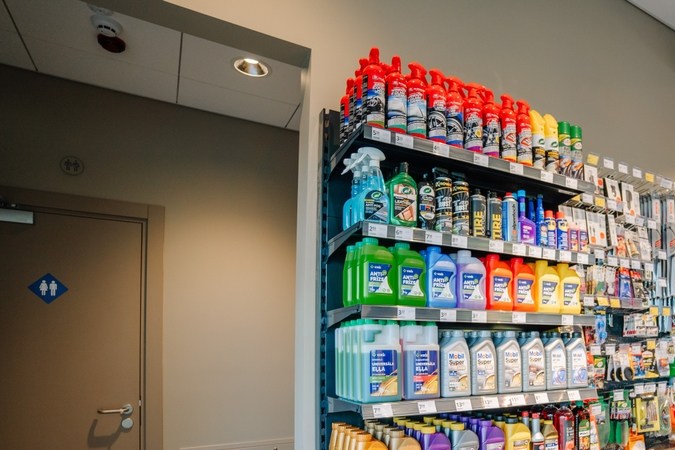 Un estante de la tienda que muestra varios productos automotrices, incluidos anticongelantes, aceite de motor y suministros de limpieza, junto a refrigerios y bebidas.