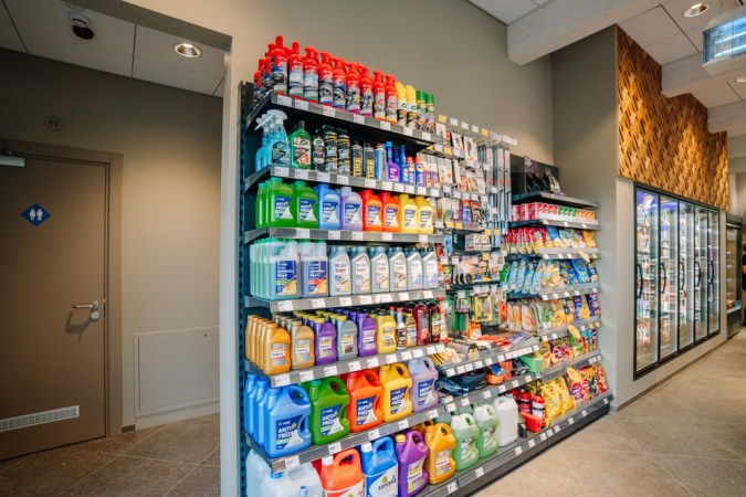 Un estante de la tienda que muestra varios productos automotrices, incluidos anticongelantes, aceite de motor y suministros de limpieza, junto a refrigerios y bebidas.