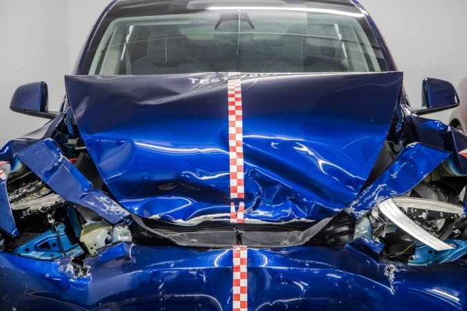 Un vehículo Tesla azul para pruebas de choque con daños graves en la parte delantera, que muestra marcas de deformación por impacto y pruebas de seguridad en un entorno controlado.