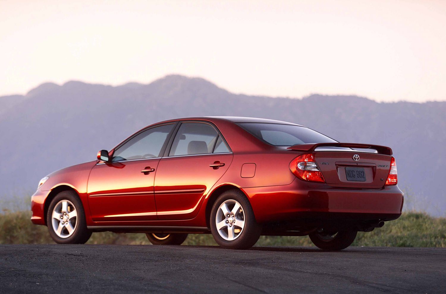 Toyota Camry 2006 rojo visto desde atrás, sedán mediano usado en carretera al atardecer.