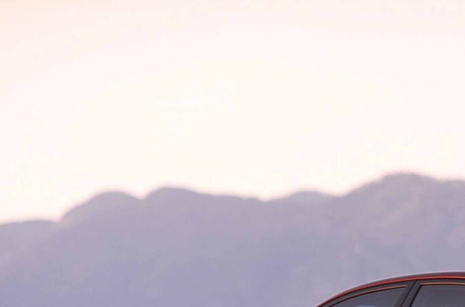 Toyota Camry 2006 rojo visto desde atrás, sedán mediano usado en carretera al atardecer.