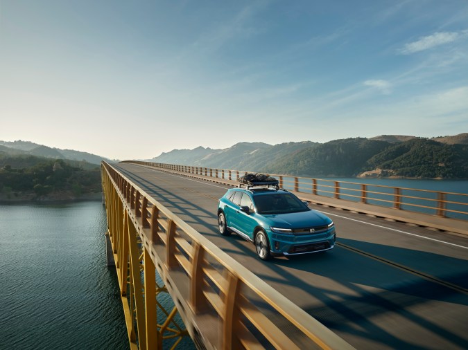 Honda Prologue Elite 2024 turquesa en carretera montañosa al atardecer, SUV eléctrico premium con equipaje, perfecto para exploración sostenible.