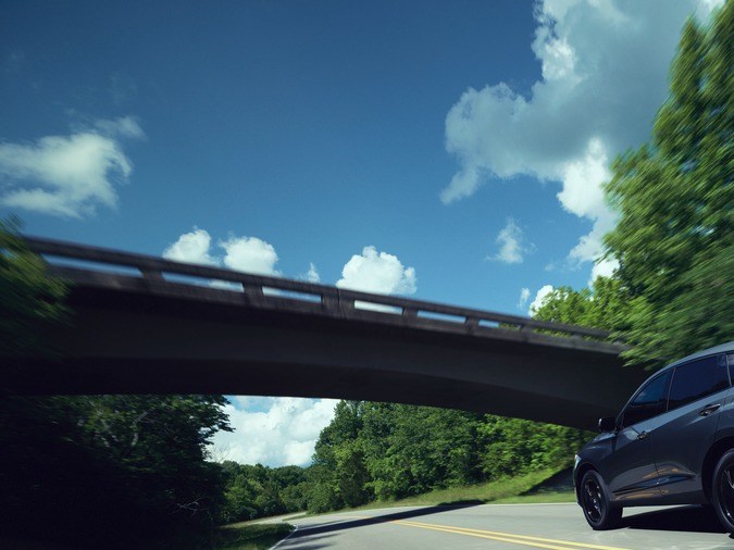 Acura RDX 2025 en carretera boscosa, acelerando con diseño deportivo y elegante