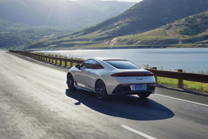 Honda Prelude 2026 blanco circulando junto al lago, coupé deportivo híbrido, perfecto para carretera, alto rendimiento, eficiencia y diseño aerodinámico para viajes largos.