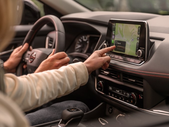 Nissan Rogue Rock Creek 2026 interior con mujer usando GPS, SUV Nissan 2026 conectividad y conducción moderna. 