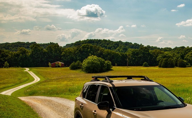 Nissan Rogue Rock Creek 2026 en color arena off-road por camino rural verde, SUV Nissan 2026 listo para aventura.