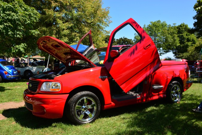 Iluminación Ford de segunda generación con puertas verticales personalizadas. Rojo Brigth con puertas y capó abiertos en una exposición local de coches aparcada en el césped.