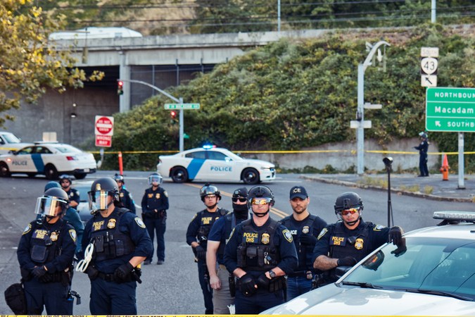 Policías de ICE se forman en fila detrás de la cinta policial en el campamento de Occupy ICE