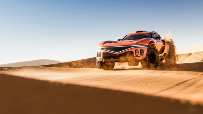 Vista del Genesis X Skorpio Concept en el desierto, con carrocería naranja, enormes neumáticos off-road, difusor y luces continuas para conducción extrema.