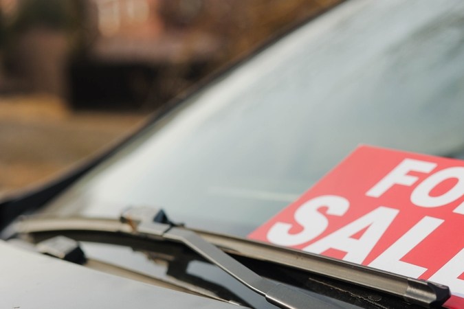 Coche en venta cartel delante del coche. Hombres poniendo su coche en venta