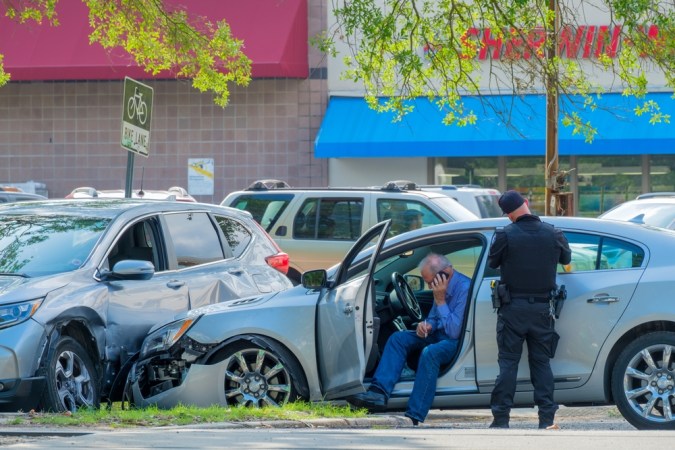 Escena del accidente automovilístico con autos dañados, policía escribiendo boletos de tráfico y conductor (en el teléfono celular) en la avenida South Carrollton.