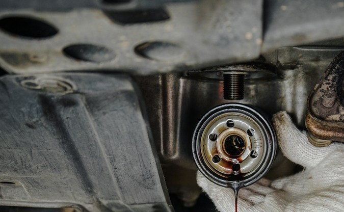 Primer plano de las manos del mecánico de automóviles que extrae el filtro de aceite inferior de un coche. Filtro de aceite usado sucio en la mano del hombre en la estación de servicio, concepto de mantenimiento del coche