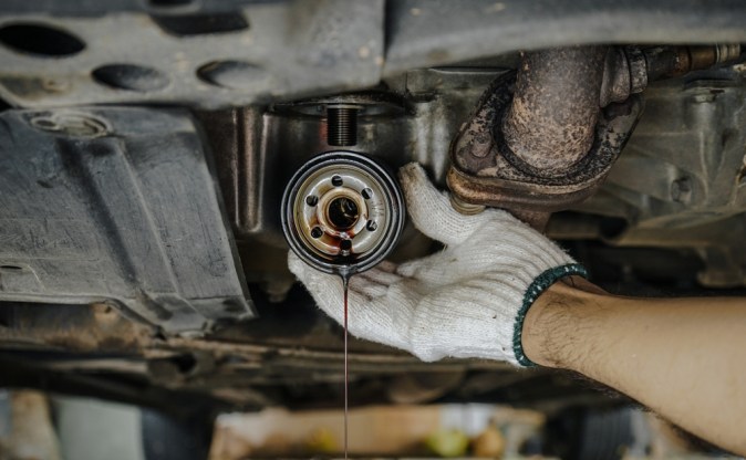 Primer plano de las manos del mecánico de automóviles que extrae el filtro de aceite inferior de un coche. Filtro de aceite usado sucio en la mano del hombre en la estación de servicio, concepto de mantenimiento del coche