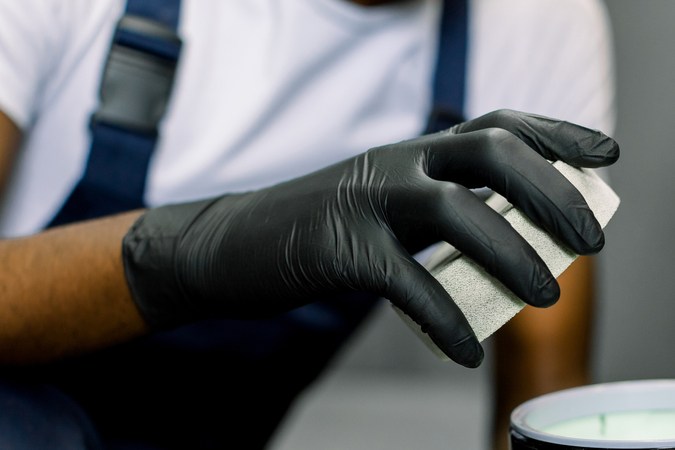 Detalle del coche, herramientas para pulir. Productos de autocuidado profesional. Cortada cerca de las manos de los trabajadores en guantes, sosteniendo el frasco con cera sólida de carnauba para pulir el cuerpo del auto