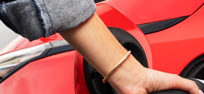 Chevy Bolt 2027 rojo cargando con conector NACS, puerto de carga visible