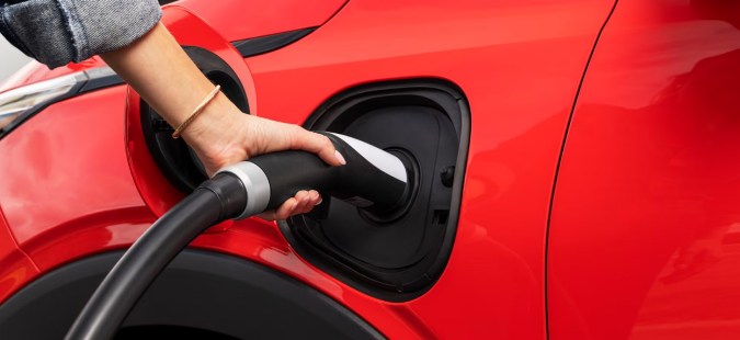 Chevy Bolt 2027 rojo cargando con conector NACS, puerto de carga visible