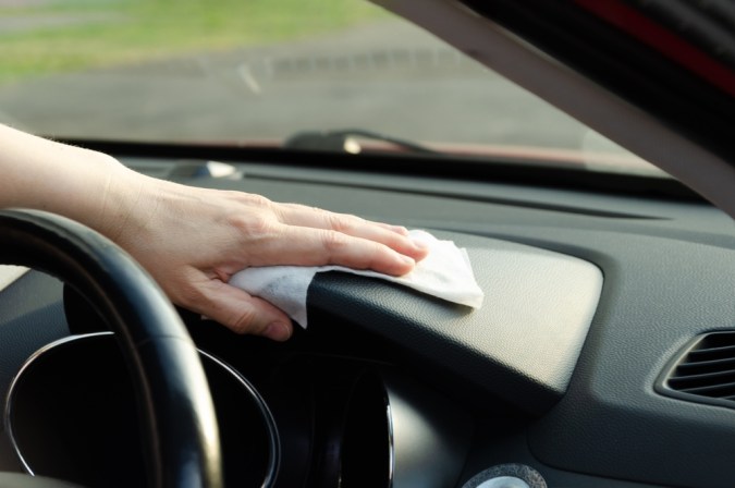 Primer plano de la mano de una mujer limpiando un panel interior del coche con una toallita. Desinfección del interior del coche.