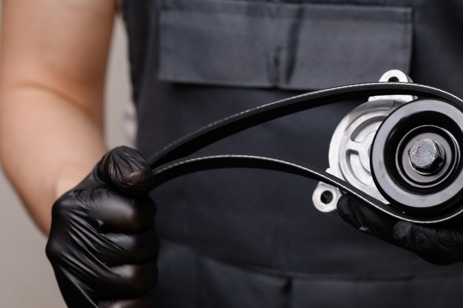 Vendedor de autopartes sostiene en sus manos una polea tensora y una correa serpentina. Reemplazo oportuno de piezas de automóviles y mantenimiento del vehículo. Venta de productos de automoción, prestación de servicios de reparación de automóviles