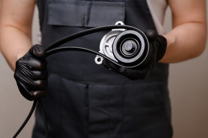 Vendedor de autopartes sostiene en sus manos una polea tensora y una correa serpentina. Reemplazo oportuno de piezas de automóviles y mantenimiento del vehículo. Venta de productos de automoción, prestación de servicios de reparación de automóviles