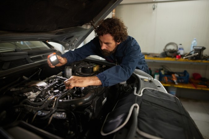 La mecánica se centra en diagnosticar y solucionar problemas del motor bajo el capó de un automóvil, utilizando una luz para inspeccionar piezas en un entorno de taller profesional