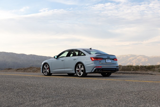 Audi S6 Sedan TDI en vista trasera gris plata, diseño deportivo elegante sobre carretera con vistas montañosas.