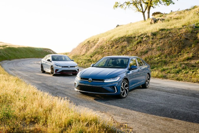 Jetta GLiI en color azul en carretera sinuosa con Jetta gris al fondo, vista exterior de autos modernos.