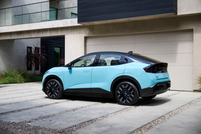 Nissan Leaf 2026 azul claro estacionado frente a garaje moderno en casa contemporánea, vista lateral trasera