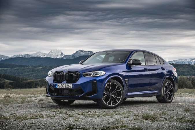 BMW X4 M foto frontal en azul Marina Bay, faros LED y placa M GmbH en paisaje alpino.