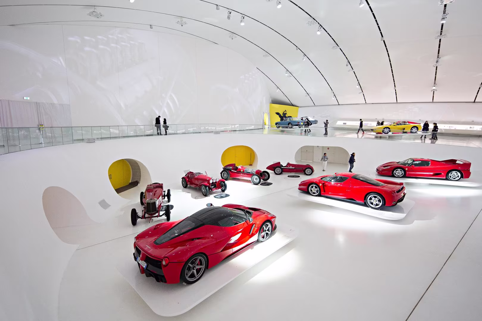 Colección de Ferrari rojos en museo futurista blanco, vista panorámica perfecta para reportajes sobre autos deportivos, tecnología italiana y experiencias en exhibiciones automotrices.