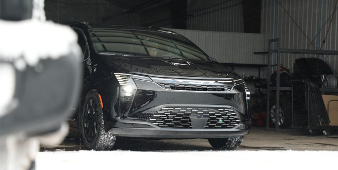 Vista frontal detallada del Chrysler Pacifica 2027 negro en garaje nevado, destacando faros verticales y parrilla renovada.