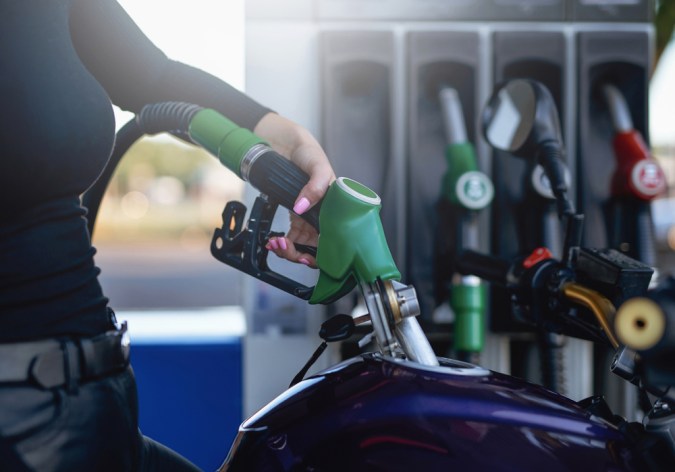 La gentil mano de la mujer está sosteniendo un arma de combustible. El tanque de la motocicleta está alimentado por la propietaria.