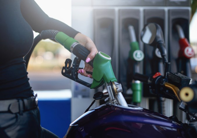 La gentil mano de la mujer está sosteniendo un arma de combustible. El tanque de la motocicleta está alimentado por la propietaria.